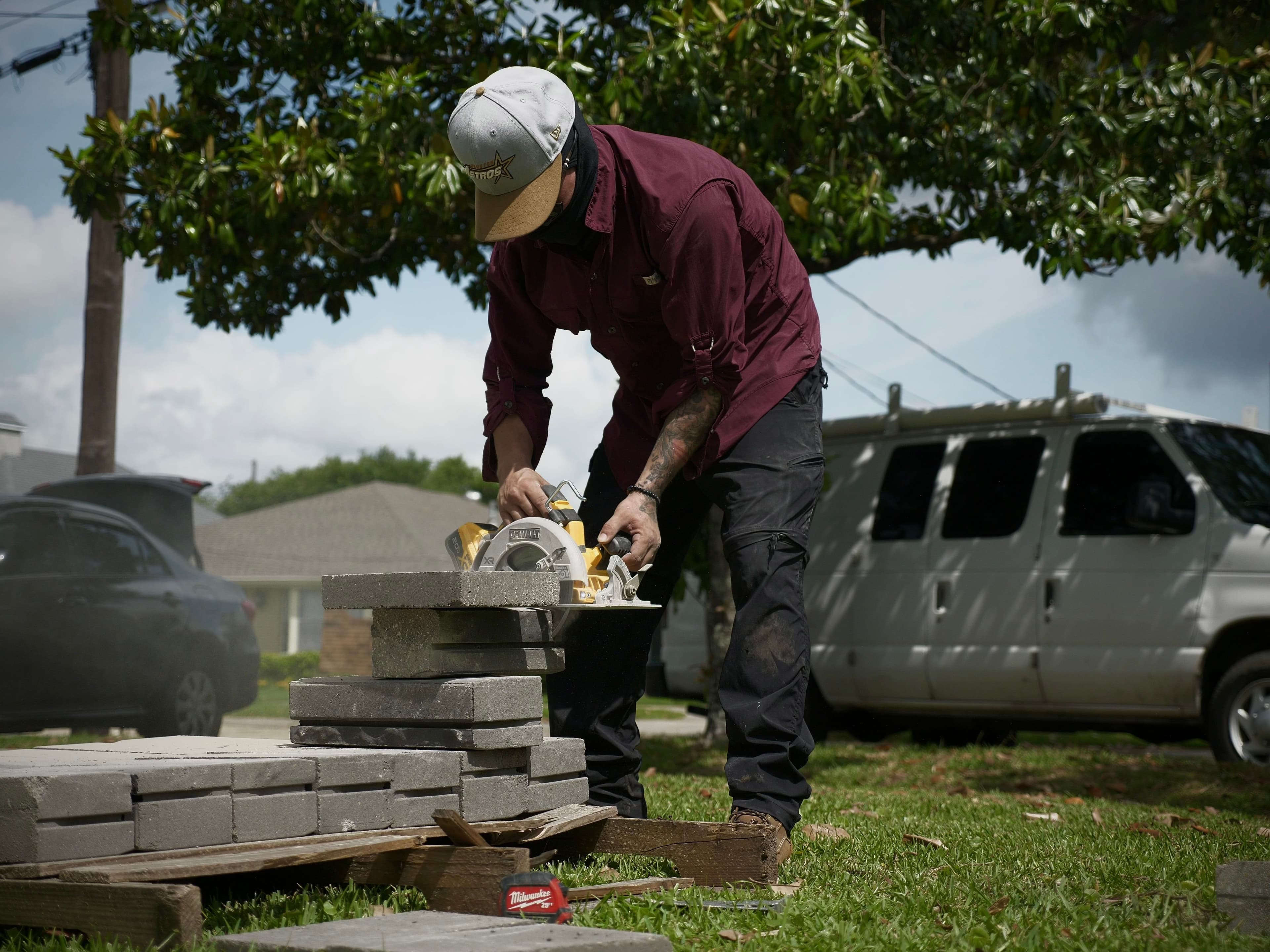 Man using a circular saw to cut stone pavers outdoors on a sunny day.
